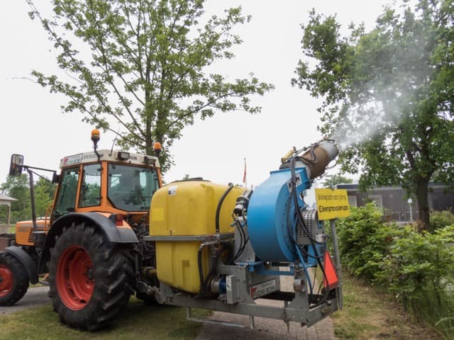 Tractor met tank en blazer voert preventieve bestrijding van de eikenprocessierups uit